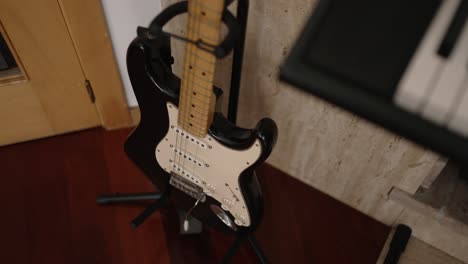 black electric guitar on a floor stand next to a keyboard inside a home music studio setup
