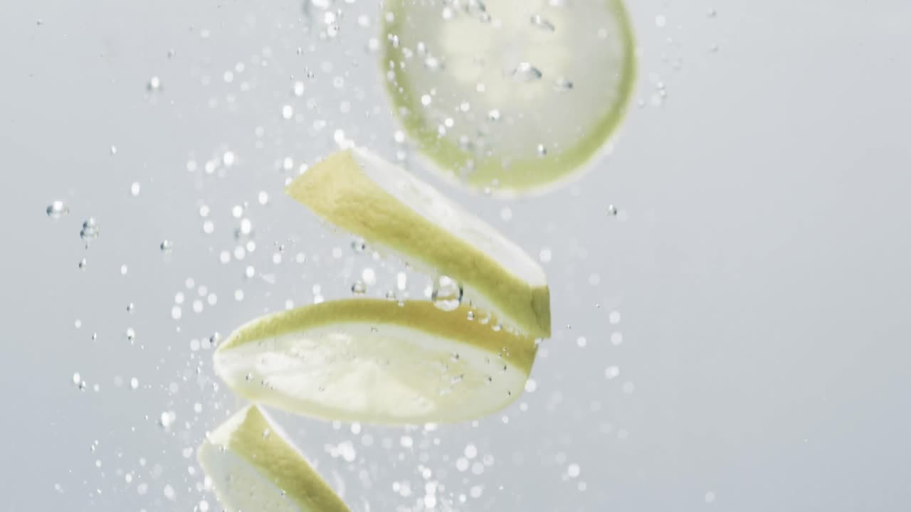 백색 배경에 복사 공간과 함께 물에 떨어지는 라임과 레몬 조각의 비디오