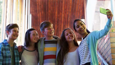 smiling schoolkids taking selfie with mobile phone in corridor