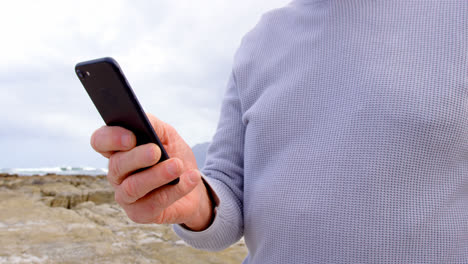 vista frontal de un anciano caucásico usando el teléfono móvil en la playa 4k