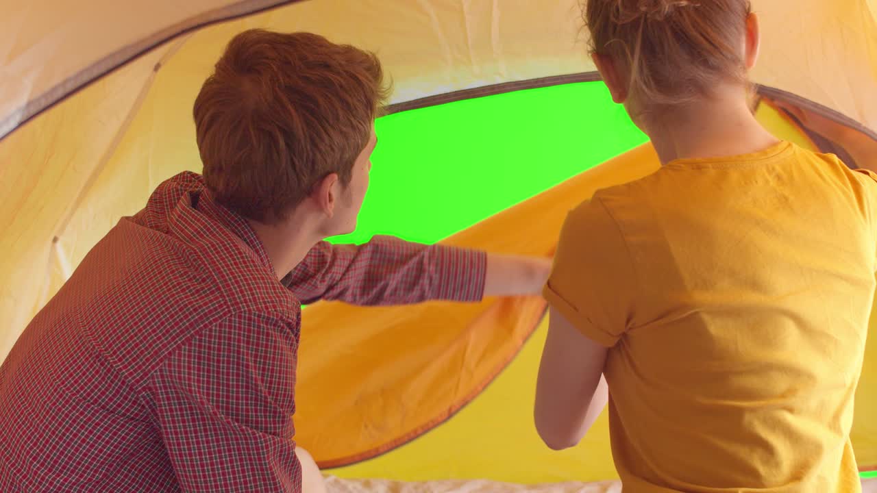 커플은 텐트를 내부에서 열고 크로마 키의 초록색 배경을 바라보고, 남자와 여자가 텐트를 열고, 크로마키, 공동 여행 개념.