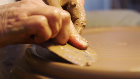 primo piano di un vasaio maschio che modella l'argilla per un piatto sulla ruota della ceramica in uno studio di ceramica