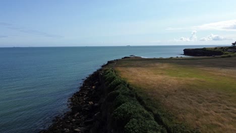 Traeth-Lligwy-idyllic-rocky-coast-shoreline-aerial-view-reversing-over-green-pasture-on-rocky-cliffs-edge