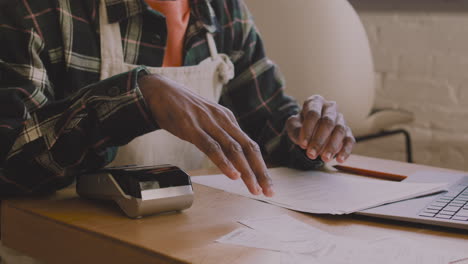 close up of an unrecognizable coffee shop owner sitting at table and calculating finance bill on laptop computer