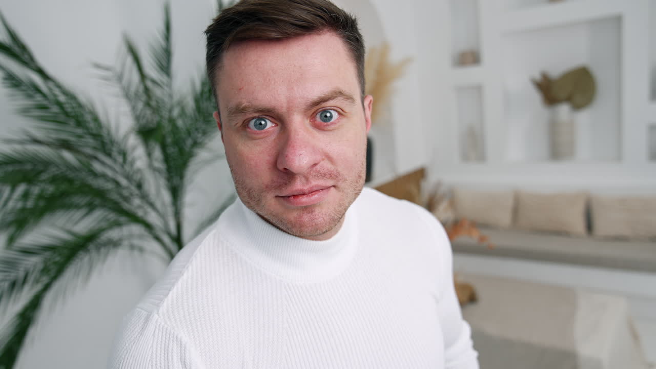 Caucasian male wearing white sweater standing near the camera. Cropped image of a man in the room. Close up.