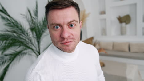 caucasian male wearing white sweater standing near the camera. cropped image of a man in the room. close up.
