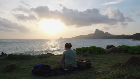 la espalda de una mujer sentada cerca de la orilla del mar durante la puesta de sol en la isla de con dao, vietnam