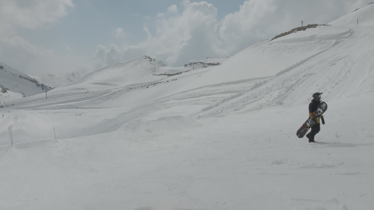 Close-up of snowboarder holding snowboard and walking uphill the pistes on the snowy slopes of Mount Hermon, Golan Heights, Israel