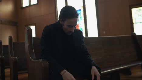 anxious, sombre man in black suit sitting in pew in church in cinematic slow motion