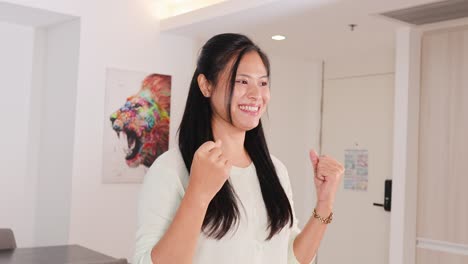 a woman in a well-lit room shows excitement with thumbs up and fist pumps, conveying a cheerful mood