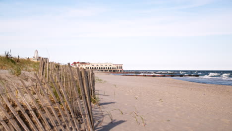 The-Distant-Ocean-City-Music-Pier-Sits-on-the-Jersey-Shoreline-with-Fence-and-Seagrass-in-foreground,-Ferris-Wheel