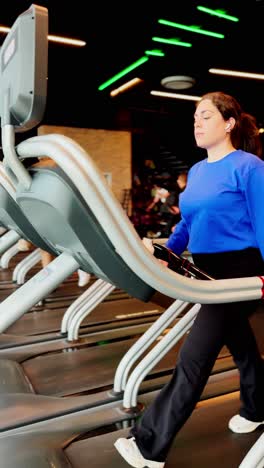Woman checking smartwatch while walking on treadmill at gym