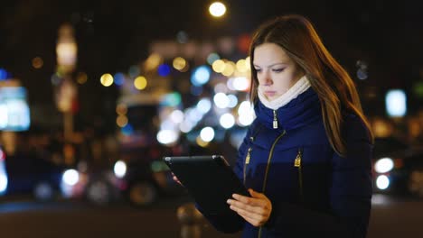 Eine-Junge-Frau-Benutzt-Ein-Tablet-Vor-Dem-Hintergrund-Der-Lichter-Der-Nachtstadt