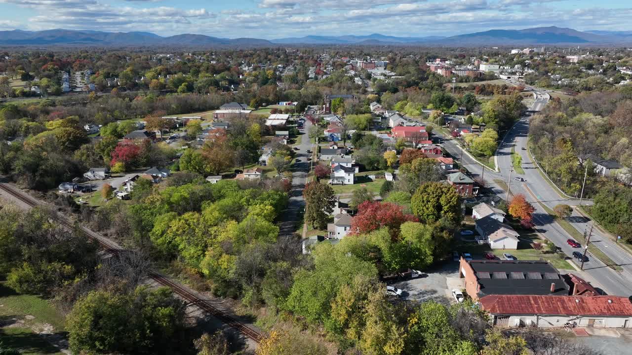 Aerial wide shot of charming city in USA with colored trees in autumn. Single family houses along street. Railway tracks of train. Virginia, USA
