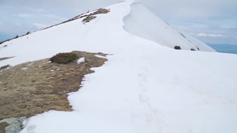 Patches-of-grass-and-rock-peek-through-snow-near-peak-of-mountain