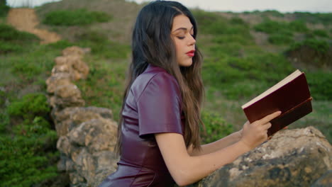 mujer lectora disfrutando de un libro sentada en la hierba rocosa colina de cerca. chica leyendo.
