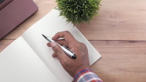 person writing in a notebook on a wooden desk with laptop