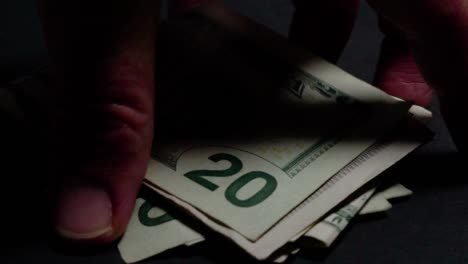 cash grab, hand picks up pile of twenty dollar bills on black background closeup