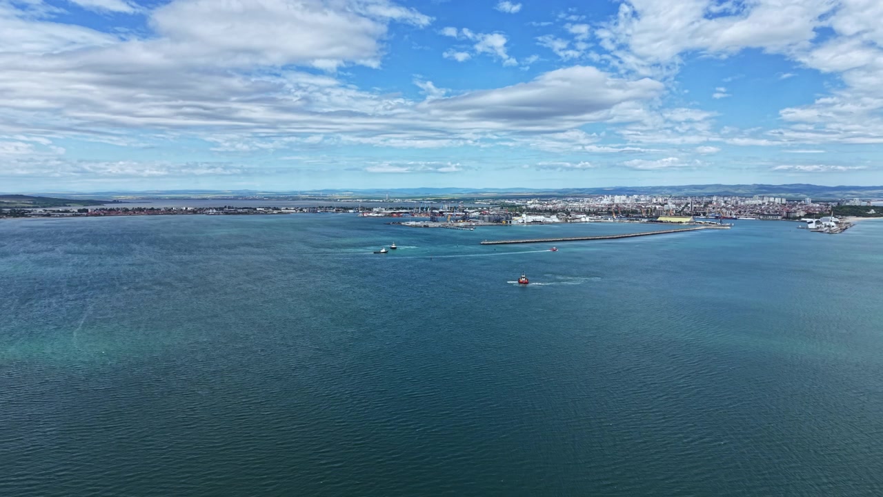 Vista di un porto trafficato con barche in acqua e skyline della città sotto le nuvole durante il giorno in una zona costiera.