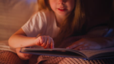 child reads story following line with finger near mother