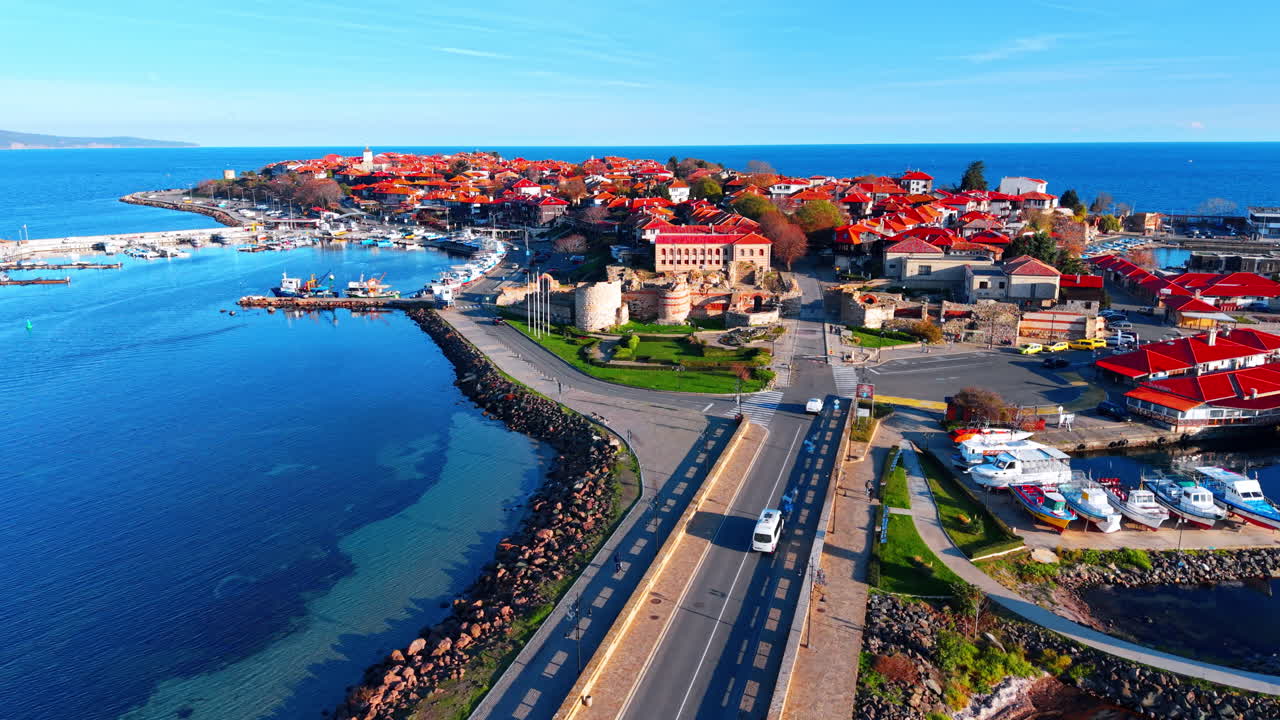 Vista ad angolo elevato dello stretto istmo e strada che conduce all'antica città di Nessebar, con case dai tetti rossi, un molo e rovine in pietra