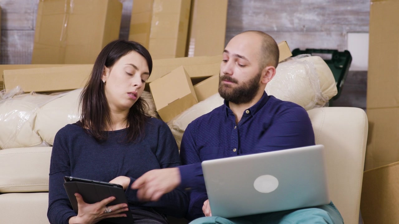 Casal sentado no chão usando laptop e tablet em casa nova
