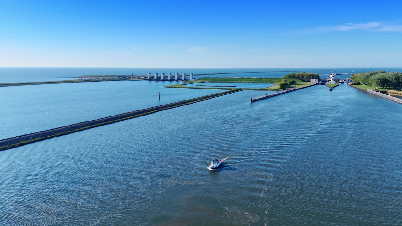Motorboat moves by the waterscape along the dam. Revealing view on the sluice at backdrop. Lelystad,the Netherlands. Aerial view.