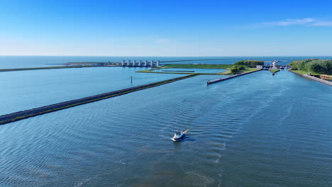 Motorboat moves by the waterscape along the dam. Revealing view on the sluice at backdrop. Lelystad,the Netherlands. Aerial view.