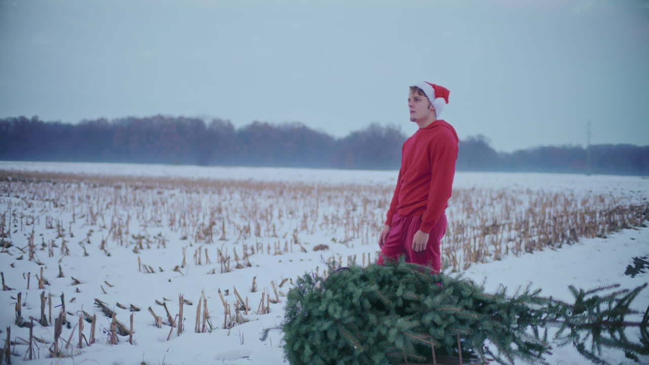 hombre pensativo de pie por el pino cortado en el paisaje cubierto de nieve durante la navidad