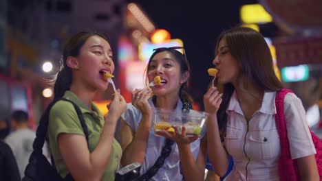 밤 시장 에서 거리 음식 을 즐기는 세 명 의 친구 들