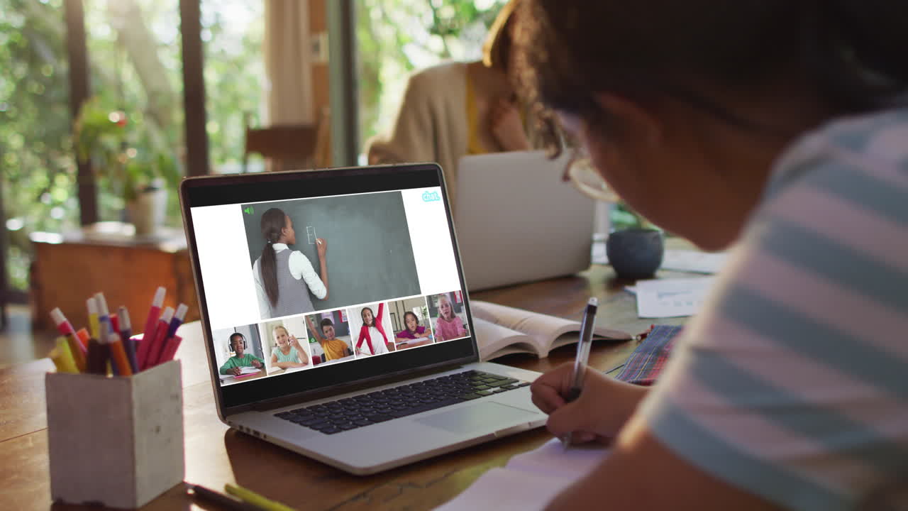 Schoolgirl using laptop for online lesson at home, with diverse teacher and class on screen