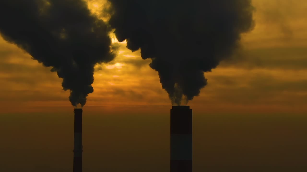 Air pollution. clouds of smoke coming from the chimneys of the plant with beautiful golden yellow lighting of setting sun. Drone flying over smoking smokestacks of a steel factory.