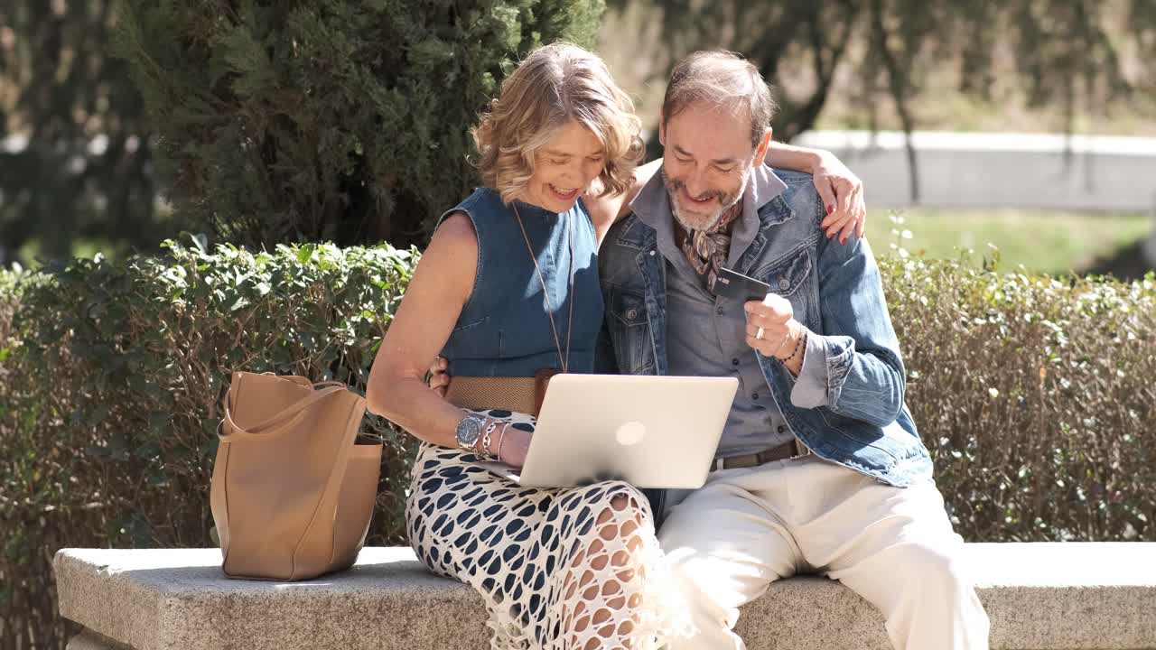 Happy mature couple using a laptop in a park
