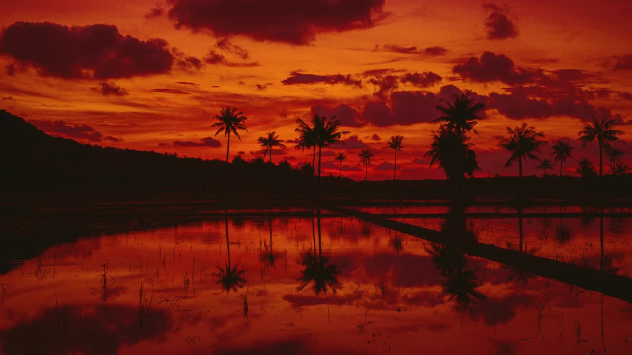 Cinemagraph /seamless video loop of rain drops falling and reflecting in the still water lagoon below a red sunset cloud sky on tropical rainforest paradise Karimun Karimunjawa island in Indonesia. 4K UHD