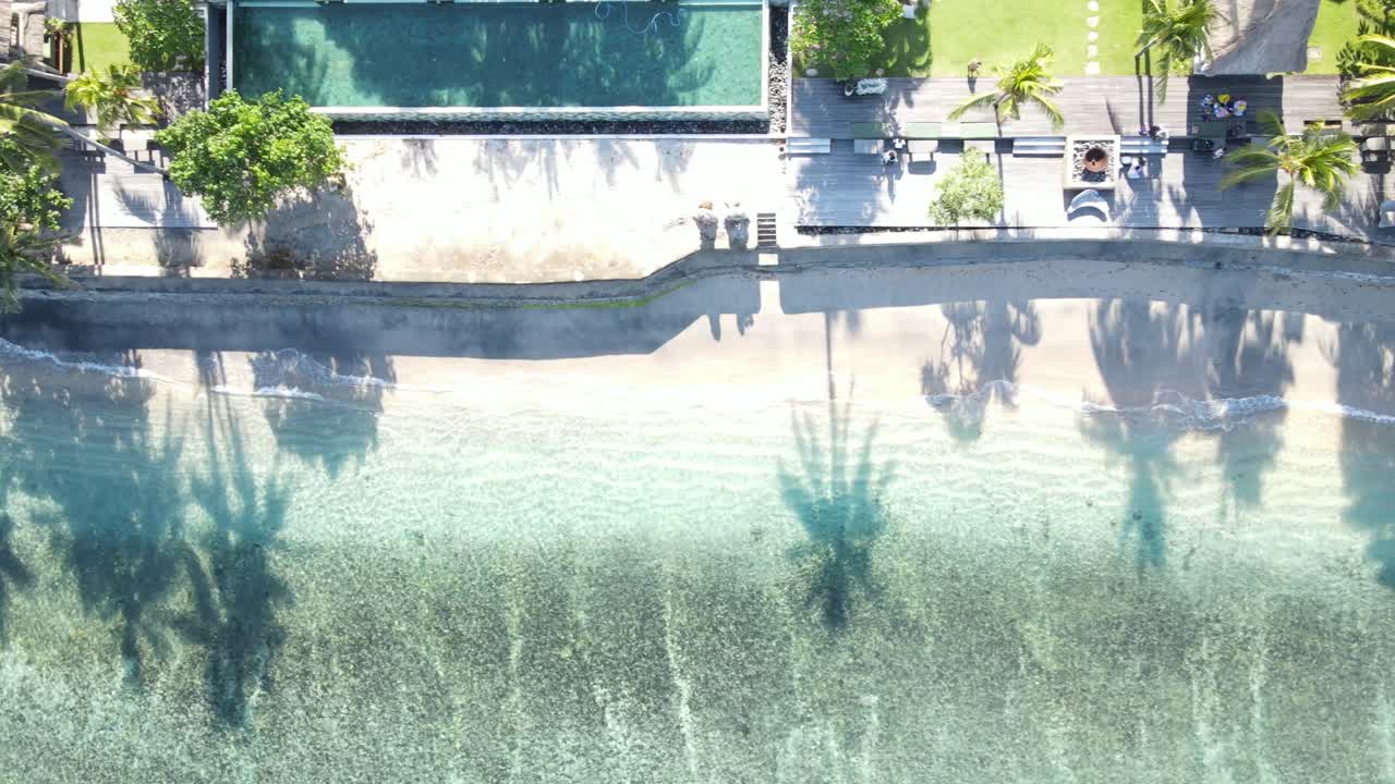 Luftfoto set ovenfra af et tropisk strandresort med klart hav og palmeskygger