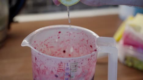 hand squeezing lemon juice into a liter measure with blueberries and raspberries, sides tainted with juice