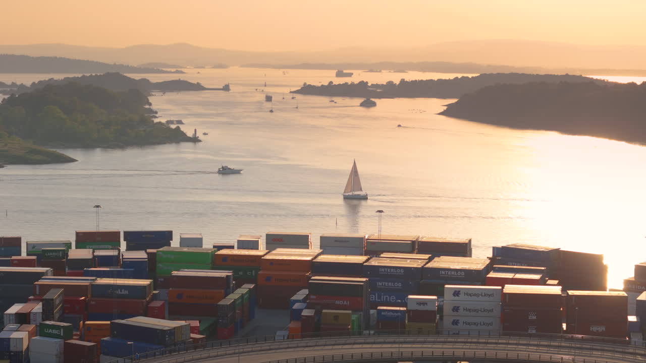 A leisure sailing boat passes Oslo Yilport container terminal at sunset