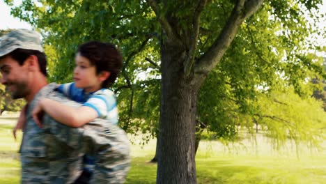 un soldado del ejército sonriente dando un paseo a cuestas a su hijo en el parque