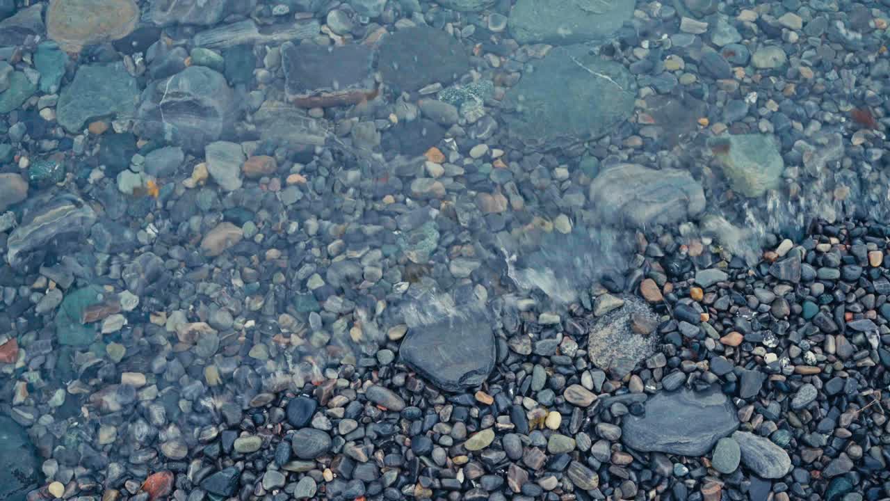 Acqua limpida scorre dolcemente su pietre lisce lungo la riva vicino a Sandland, municipalità di Loppa, Finnmark, Norvegia - Primo piano