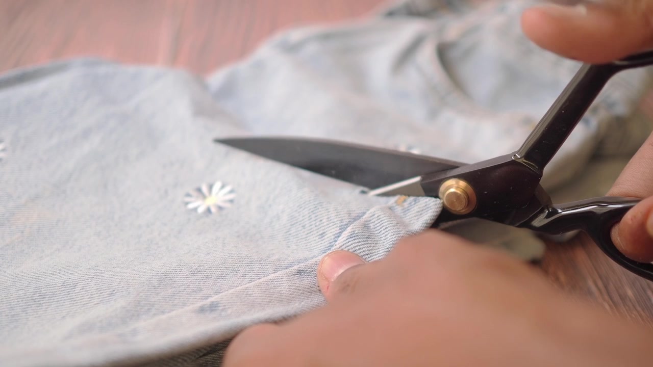 Person Cutting Denim Fabric with Scissors on Wooden Table