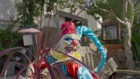 small scary clown doll sitting next to a plant