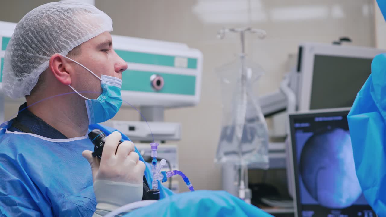 Doctor in medical uniform doing endoscopy. Side view of a surgeon working with new medical equipment in operating room. New technologies in medicine.