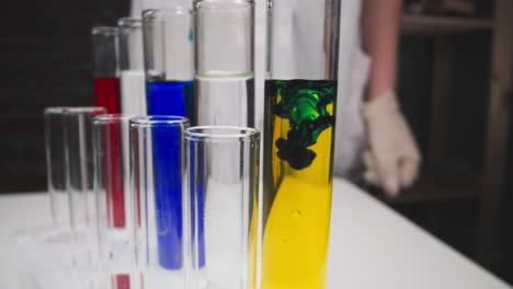 chemists drips reagent into test tube with yellow liquid