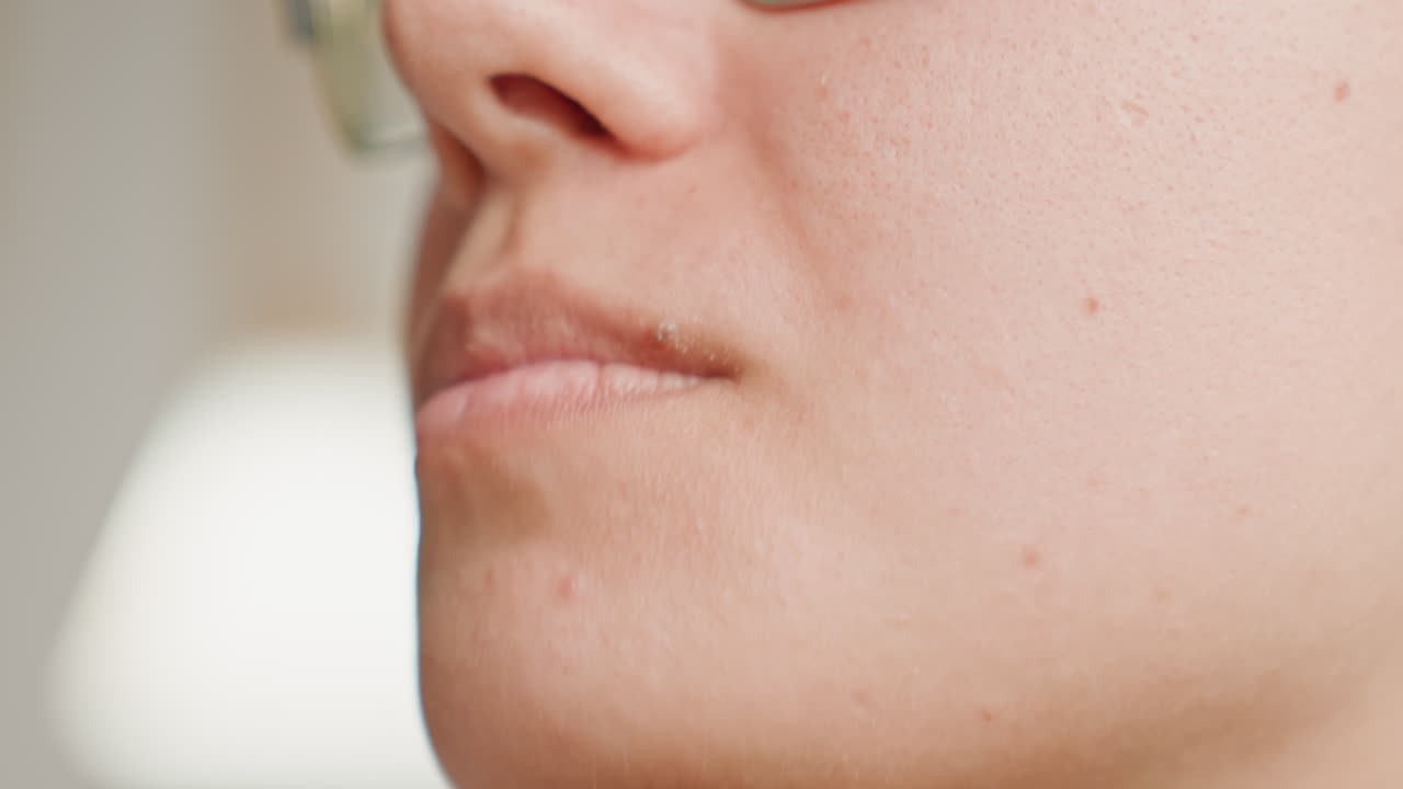 Primo piano di donna che assaggia con un cucchiaino in camera d'albergo, scena contemplativa della colazione con ospite che assaggia il cibo, labbra leggermente increspate e masticazione sottile, montatura degli occhiali, luce calda interna, dettaglio della texture della pelle, focalizzata.