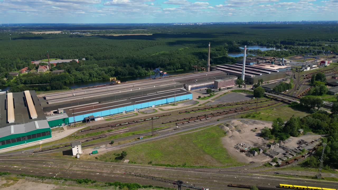 Hennigsdorf steel factory with chimneys, warehouses, railway, near river and forest in summer. Nice aerial view flight fly push forward drone