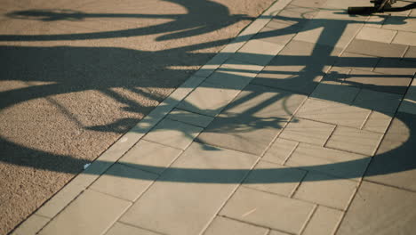 shadow of upside-down bike cast on ground pavement, with visible back tire rotating, creating a dynamic silhouette effect in warm sunlight