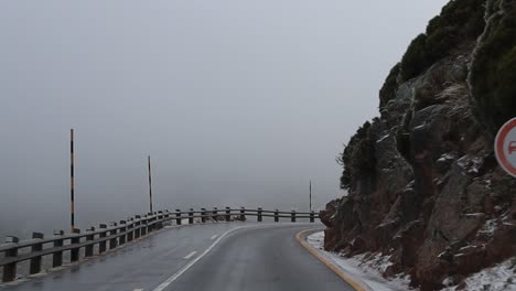 driving on a  wet snowy mountain road with jagged cliffs taking sharp turns on a foggy day with low visibility