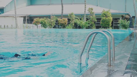 Junge-Asiatische-Schwimmerin-Im-Schwarzen-Badeanzug-Und-Schwimmbrille-Benutzt-Leitern,-Um-Aus-Dem-Schwimmbad-Zu-Kommen