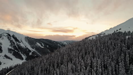 drone aerial footage flying over rocky mountains alpine pine tree mountain valley slopes during beautiful golden hour sunset in loveland pass, colorado