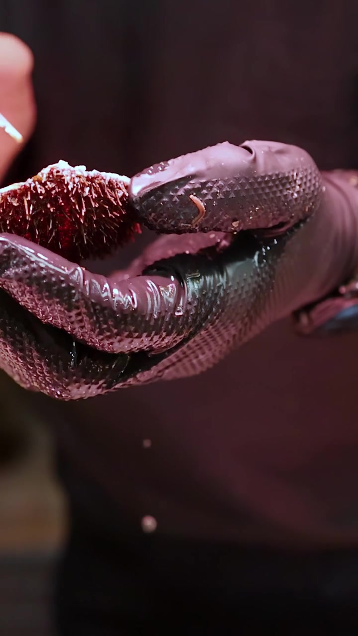 Primo piano delle mani dello chef che usano le pinzette per pulire uni crudo in un mercato del pesce giapponese